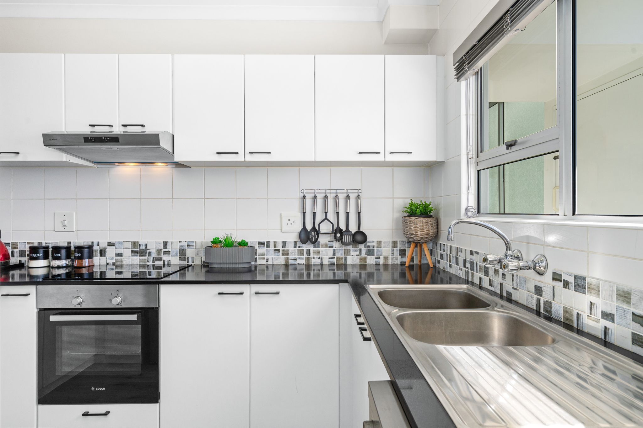A modern kitchen with white cabinets, a Bosch oven, a double sink, and a window with a view.