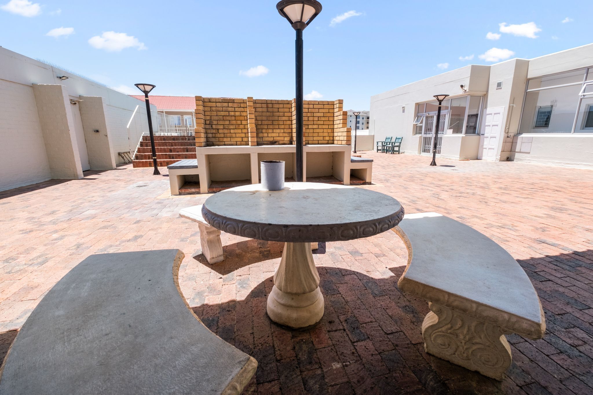 A courtyard with a round table and benches, brick walls, and a staircase.