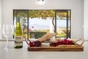 A table with a bottle of wine, a glass, a baguette, cheese, grapes, and a fruit bowl.
