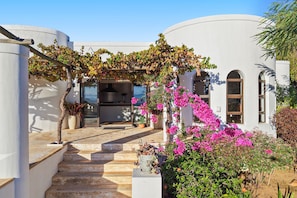 A white building with a covered entrance, steps leading up to a door, and a garden with pink flowers. - Riebeek-kasteel Villa (Riebeek Kasteel)