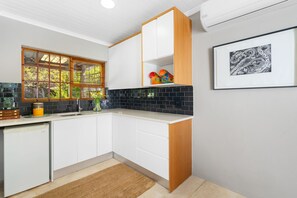 A modern kitchen with white cabinets, a black tiled backsplash, and a window with a view of greenery.