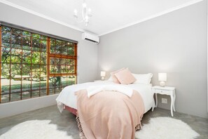 A bedroom with a large window, a bed with white and pink bedding, a white nightstand, and a white furry rug. - Riebeek-kasteel Villa (Riebeek Kasteel)