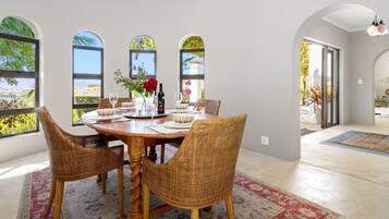 Un comedor con una mesa redonda, sillas de mimbre y vistas amplias a través de grandes ventanales.
