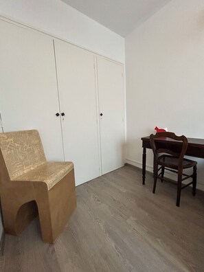 A room with a wooden floor, a brown chair, a wooden table, and a white wardrobe. - COSY Concarneau (Concarneau)