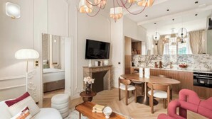 A modern living room with a sofa, a coffee table, and a TV. There is a dining area with a wooden table and chairs. The kitchen has a marble countertop and modern appliances. - JUST MOMENTS FROM THE ICONIC CHAMPS-ÉLYSÉES & AVENUE MONTAIGNE - 2 BEDROOM (Paris)