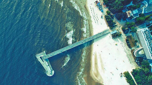 Vue aérienne d’une zone côtière avec un pont, une plage et des bâtiments adjacents.