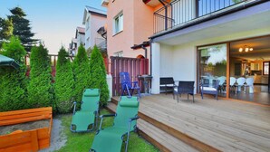 Une terrasse en bois avec des sièges extérieurs, une porte d’entrée en verre et une vue sur l’intérieur.