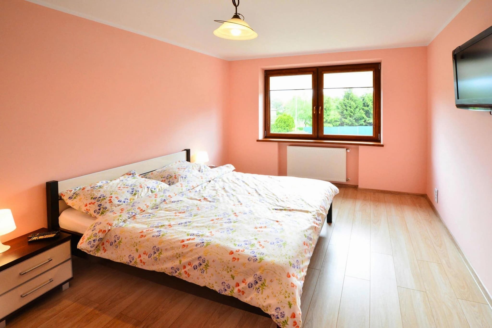 A bedroom with a bed, a nightstand, a lamp, a window, and a television.