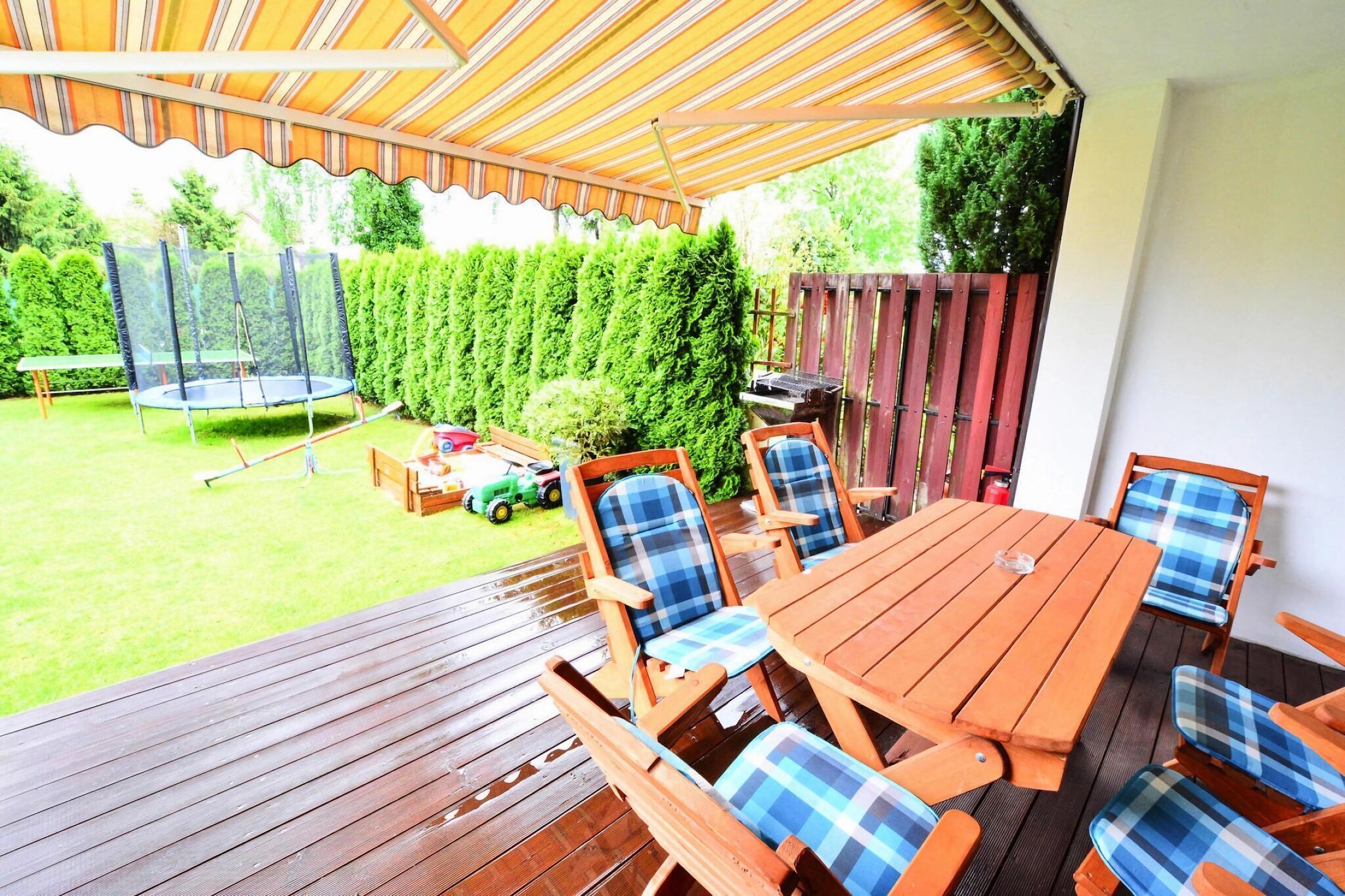 An outdoor patio with a wooden table and chairs, a trampoline, and a grill area.