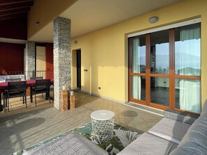 A sunlit patio with a dining area, a stone pillar, and a large sliding glass door leading to a balcony. - Apartment La Terrazza (Cannero Riviera)