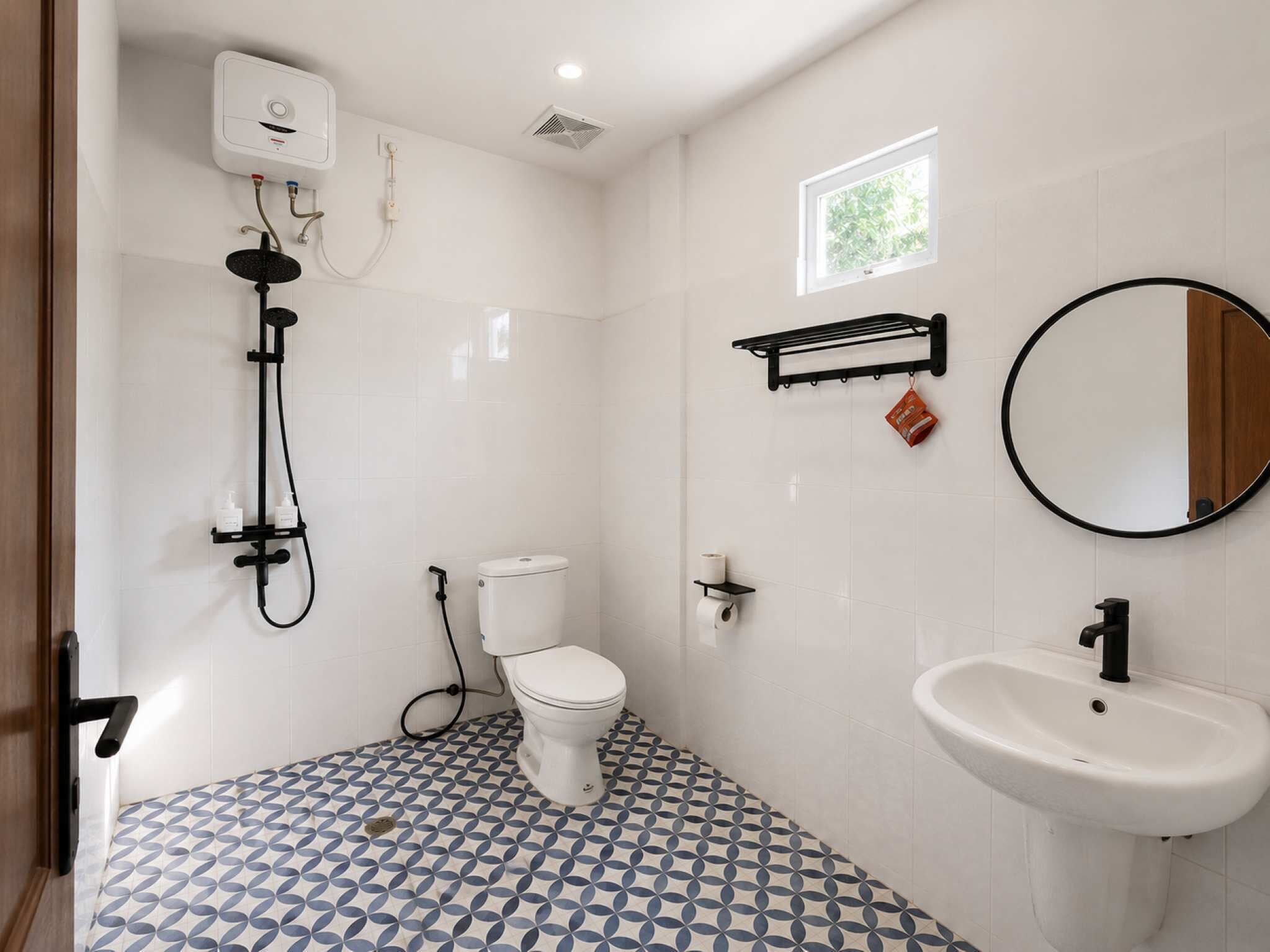 A bathroom with a toilet, bidet, and sink, with patterned floor tiles and a small window.