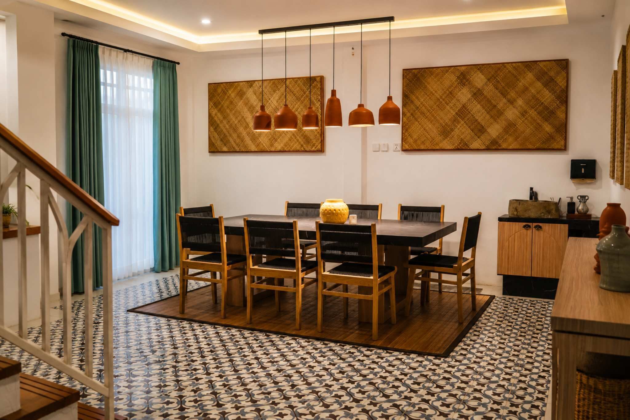 Un comedor con mesa, sillas, lámparas colgantes y obras de arte en las paredes.