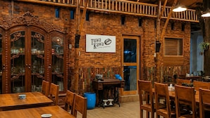 A restaurant interior with brick walls, wooden furniture, and a sign for 'Tuwa Kawa Coffee & Roastery.'