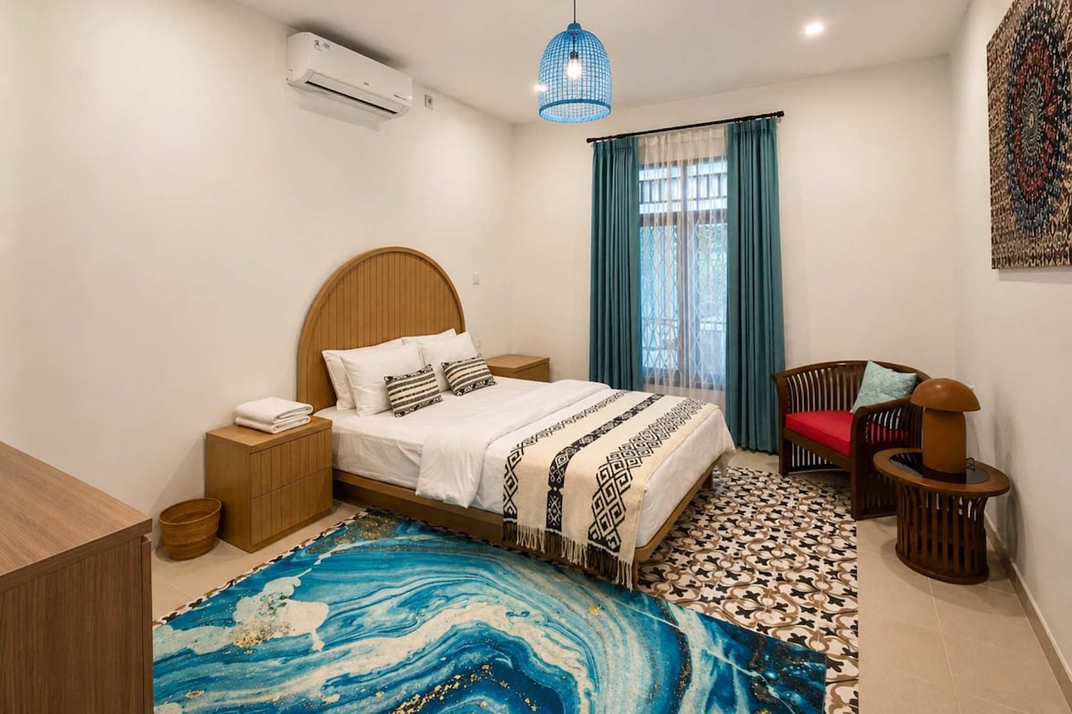 A modern bedroom with a bed, bedside table, lamp, chair, and a decorative rug.
