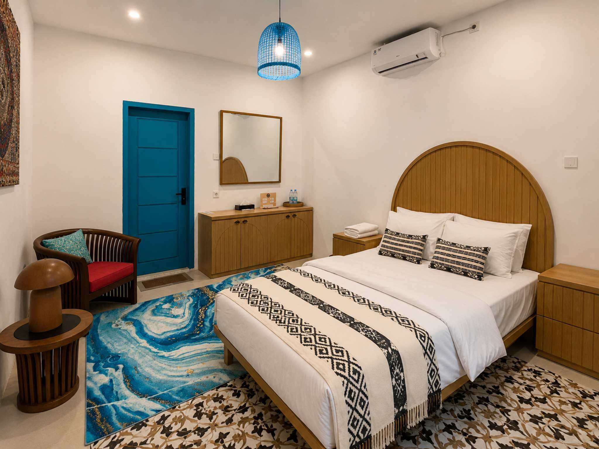 Ein Schlafzimmer mit einem Bett, einer blauen Tür, einer Holzkommode, einem Nachttisch, einem Spiegel und einer blauen Pendelleuchte.