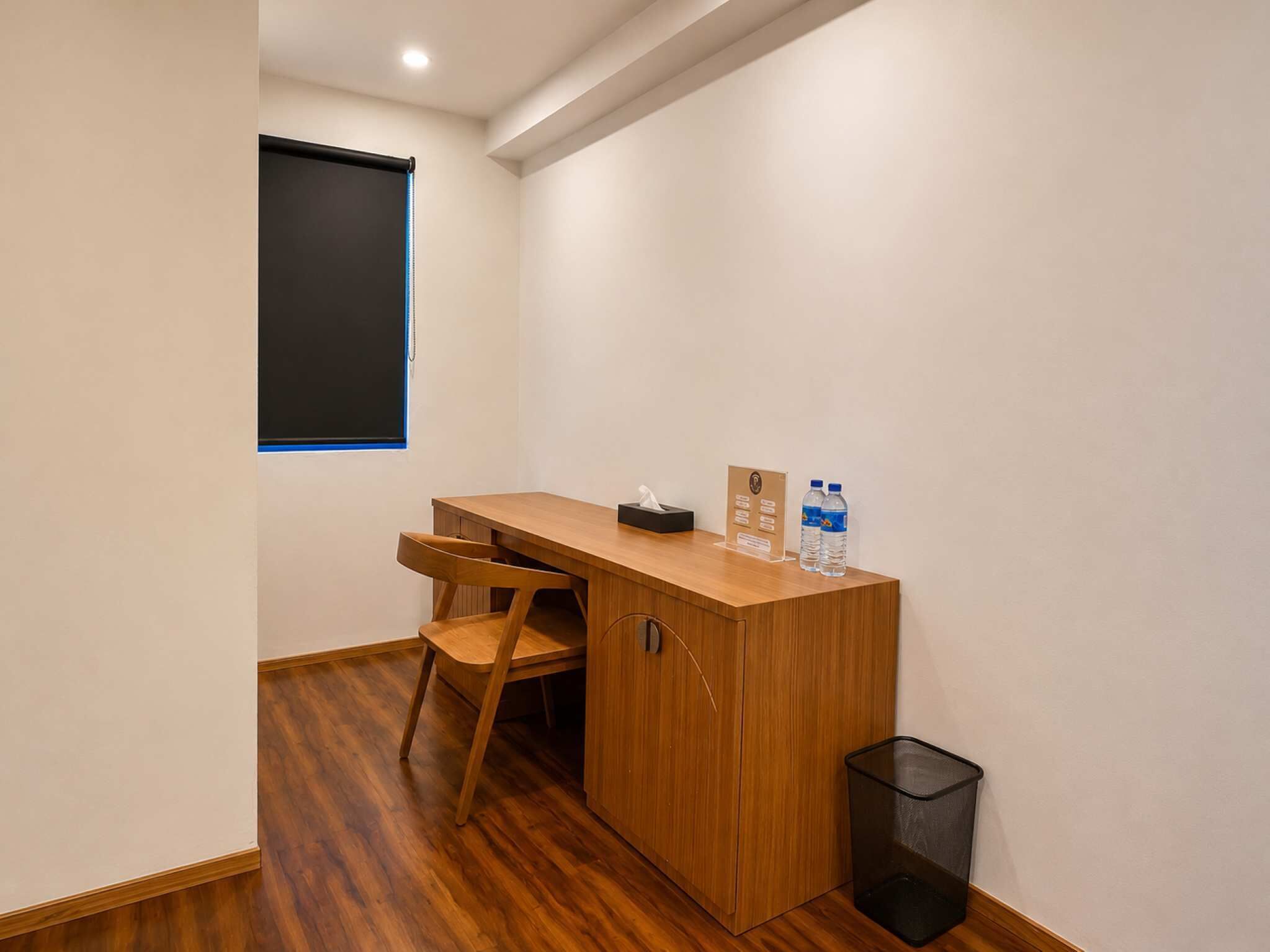 Un petit bureau privé, avec un bureau en bois, une chaise, une corbeille et une fenêtre équipée de stores.