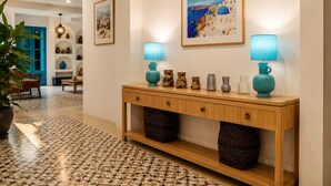 A hallway with a patterned floor, a wooden console table with decorative vases, a framed painting, and a blue lamp.