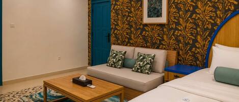 A hotel room with a sofa, a bed, a wooden table, a blue door, and a patterned wall.