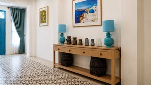 A hallway with a wooden console table, two blue lamps, a patterned rug, and framed pictures on the walls.