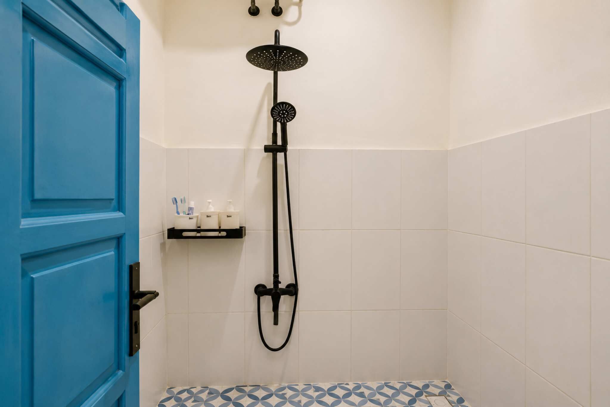 Casa de banho com porta azul, chuveiro com duche manual e prateleira com artigos de higiene pessoal.