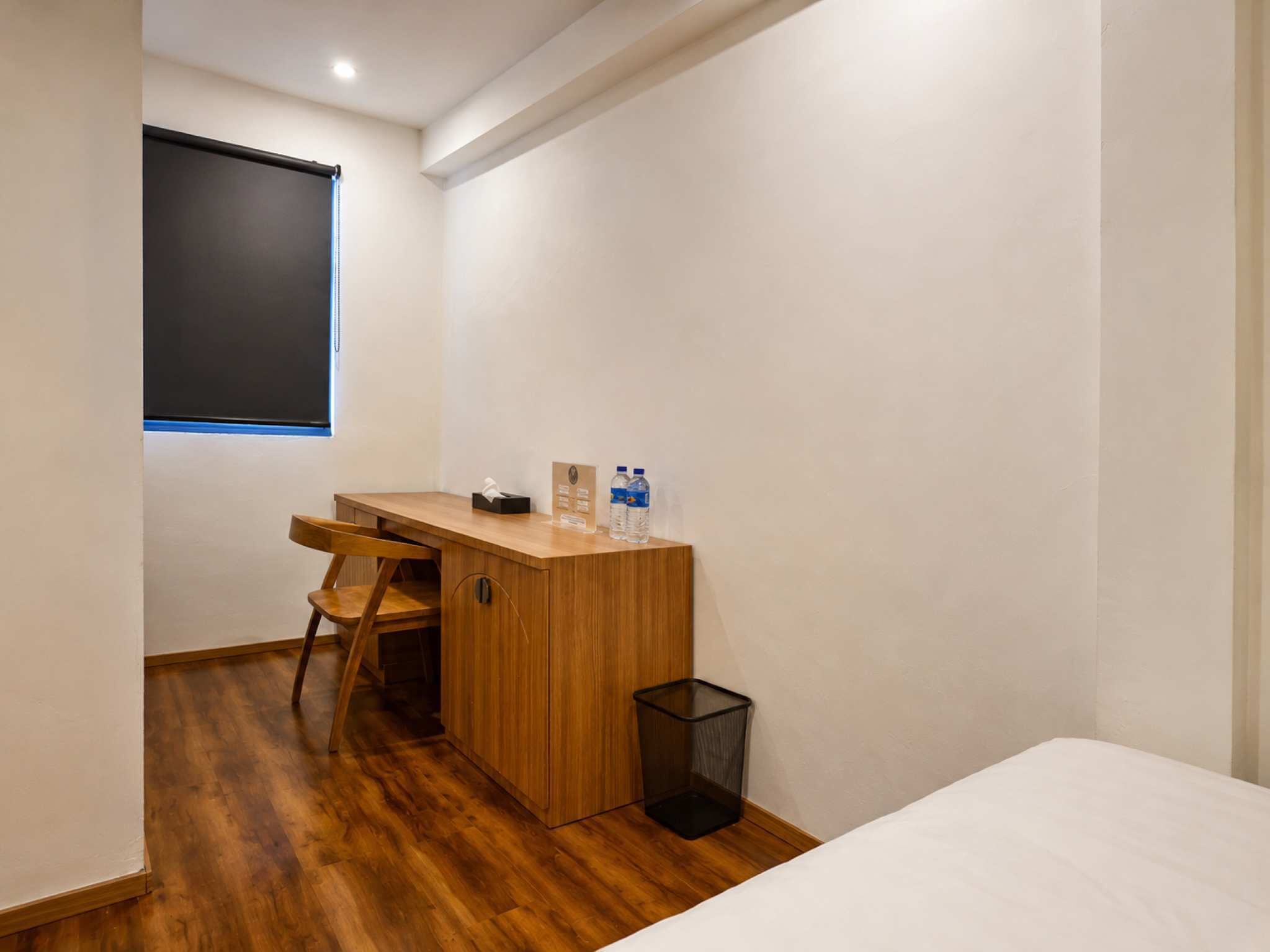 A small, neatly arranged bedroom with a wooden desk, a chair, a bed, and a window.