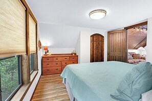 A bedroom with a large bed, wooden dresser, and a view of the outdoors through a window. - Clutter Falls Retreat with Two Homes, Hot Tubs & Guadalupe River Views (New Braunfels)