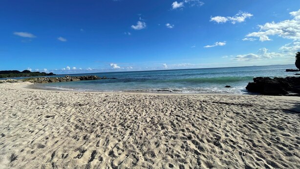 Een zandstrand met helderblauw water en enkele bewolkte luchten.