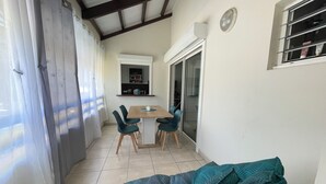 Een kamer met een eettafel en stoelen, een bank, een schuifdeur met glas en een raam.