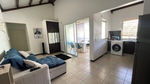 Een kleine woonruimte met een bank, een wasmachine en een eethoek met tafel en stoelen.