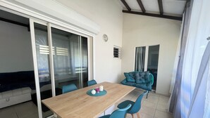 Een eethoek met een houten tafel, blauwe stoelen en een glazen schuindeur naar een balkon.