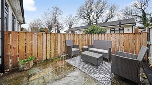 Een terras met rieten meubilair, een kamerkleed met dessin en een houten omheining.