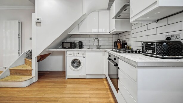 Een kleine keuken met witte kastjes, een ingebouwde wasmachine, een magnetron en een fornuis.