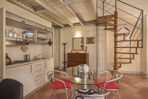 A compact kitchen with modern appliances, a dining area with a glass table and metal chairs, and a wooden spiral staircase. - Bargello 121 Apartment (FIRENZE)