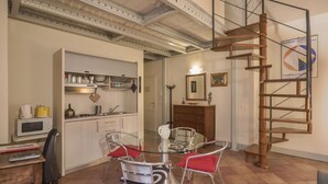A compact kitchen with a glass dining table, a wooden staircase, and a kitchen counter with appliances.