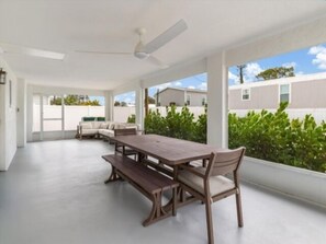Un vaste patio doté d’une table et de bancs en bois, de grandes fenêtres offrant une vue sur les maisons voisines et d’un ventilateur de plafond.