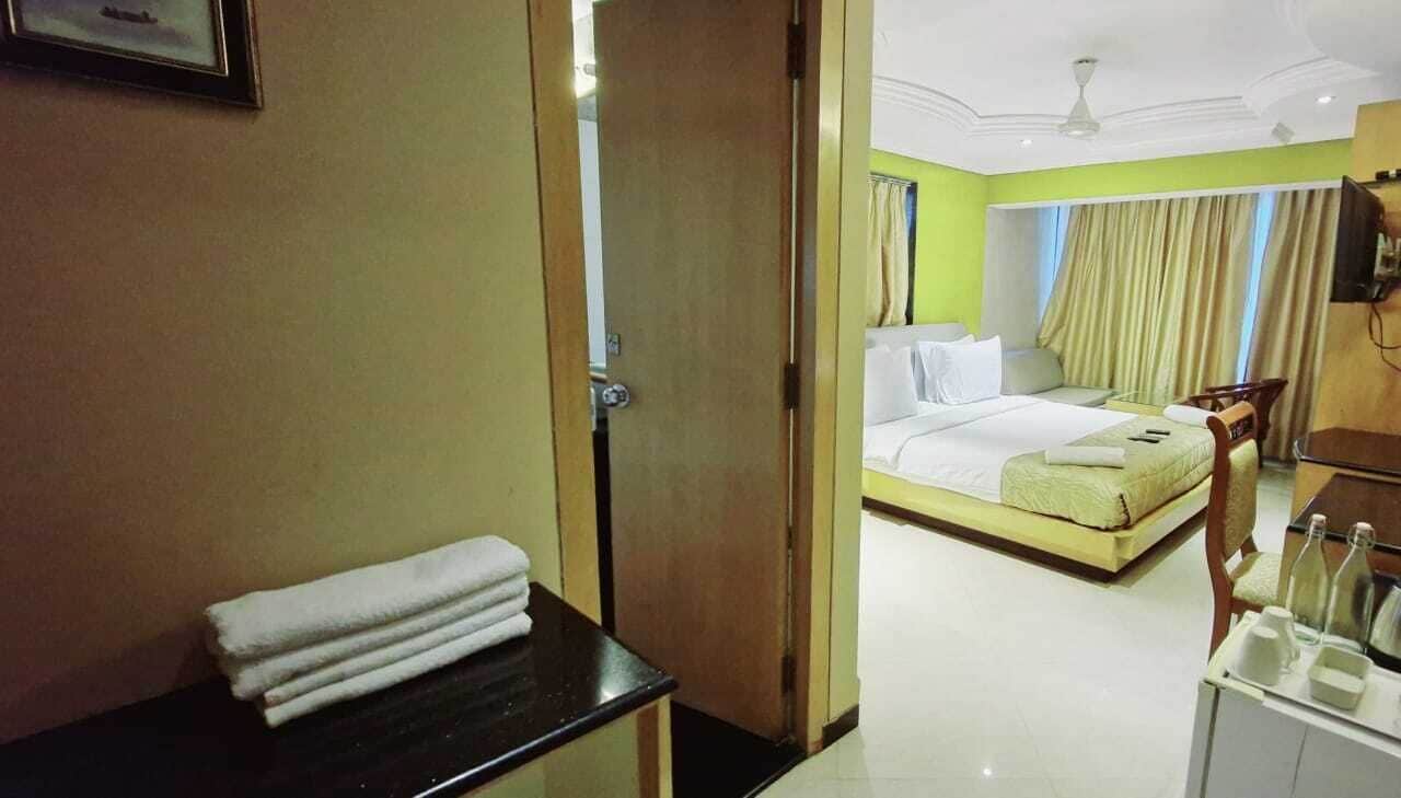 A hotel room with a bed, a bedside table with a towel, a desk with a chair, and a TV.