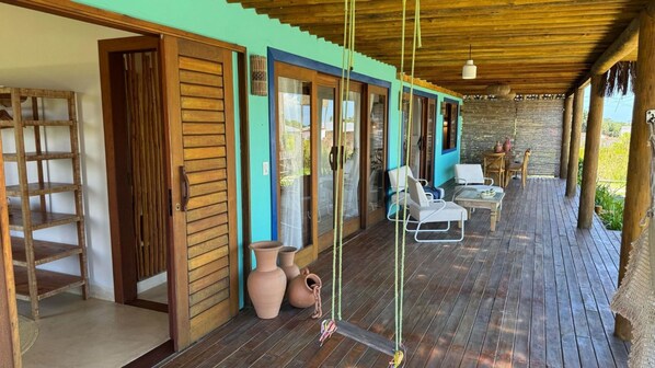 A wooden deck with outdoor seating, a wooden door, and a view of the garden. - Casa Pindorama com Vista Para o mar em Corumbau (Prado)