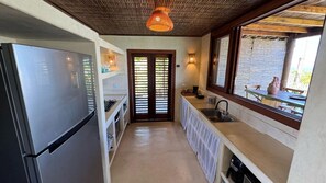 A narrow kitchen with a refrigerator, a sink, and a window overlooking a patio. - Casa Pindorama com Vista Para o mar em Corumbau (Prado)
