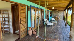 A wooden deck with outdoor seating, a wooden door, and a view of the garden. - Casa Pindorama com Vista Para o mar em Corumbau (Prado)