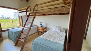 A room with bunk beds, a ladder, a bedside table with a vase, and a window with a view of greenery. - Casa Pindorama com Vista Para o mar em Corumbau (Prado)