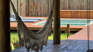 A hammock hanging between wooden posts, a wooden deck, and a pool area with a wooden fence in the background. - Casa Pindorama com Vista Para o mar em Corumbau (Prado)