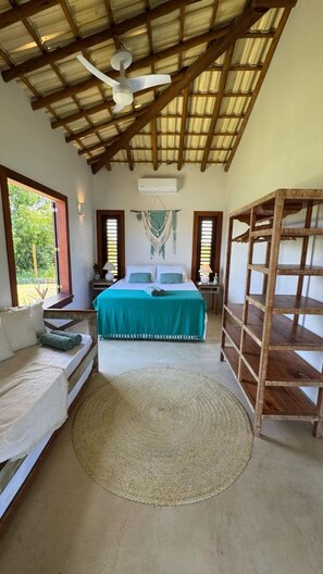 A bedroom with a bed, a wooden shelf, a woven rug, and a ceiling fan. - Casa Pindorama com Vista Para o mar em Corumbau (Prado)
