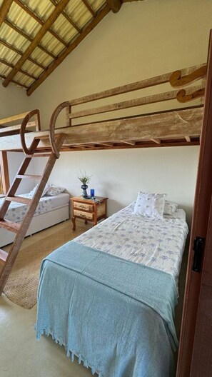 A bedroom with a bunk bed, a wooden ladder, a bedside table with a plant, and a bed with a patterned bedspread. - Casa Pindorama com Vista Para o mar em Corumbau (Prado)