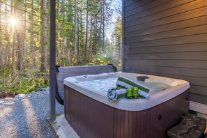 Ett bubbelbad med ett handduk och två ölburkar, omgivet av en skog.