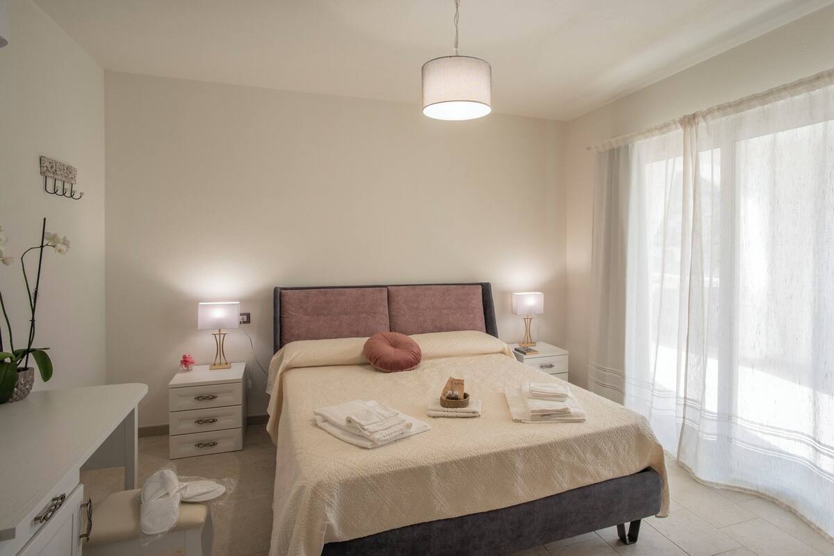 A bedroom with a bed, bedside tables, a desk, and a window with curtains.