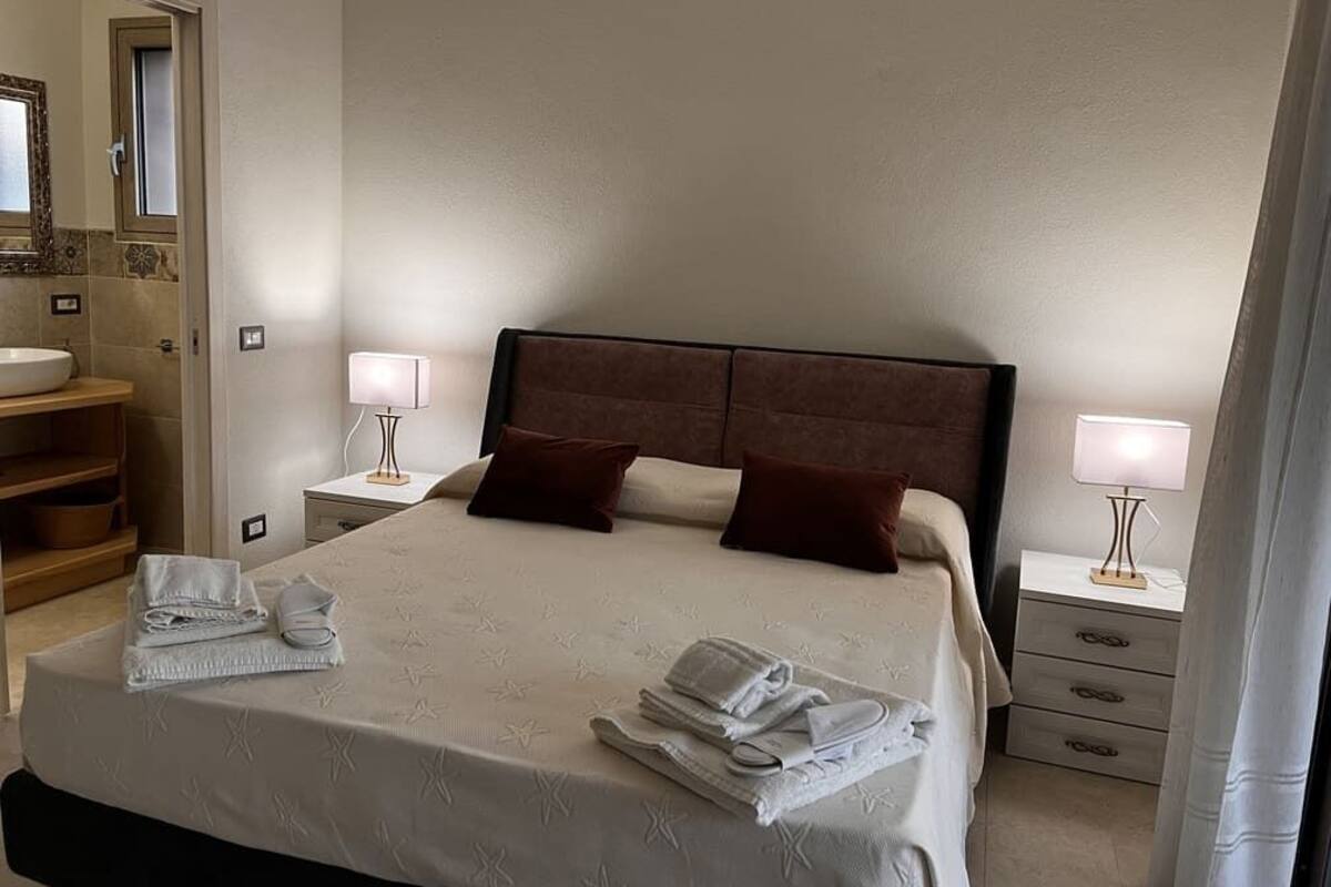 A neatly made bed with pillows, a bedside lamp, and a folded towel on the nightstand.