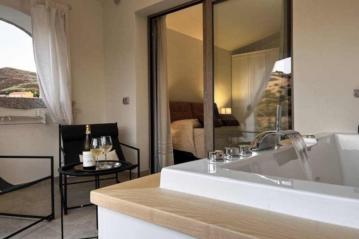 A modern bathroom with a large bathtub, a small table with a bottle and glasses, and a chair.