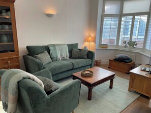 A cozy living room with a green sofa, a wooden coffee table, and a lamp. - Seahorse Cottage (Weymouth)