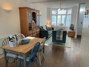 A dining area with a wooden table and chairs, a cabinet with glass doors, a sofa, and a television on a wooden stand. - Seahorse Cottage (Weymouth)