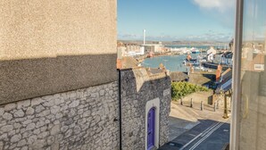 A stone building with a purple door, overlooking a harbor with boats and buildings. - Seahorse Cottage (Weymouth)